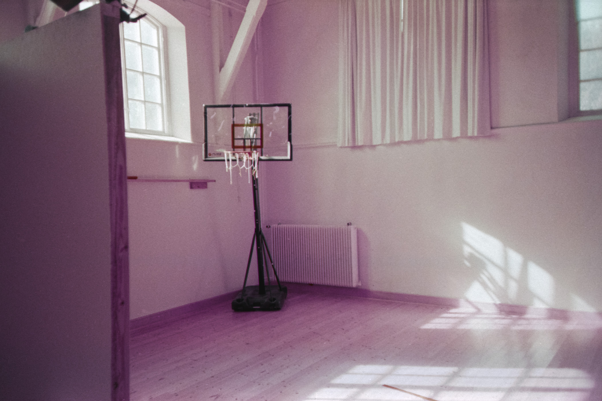 Proselytization — a portable basketball hoop bathed in warm morning light through tall windows, Skåne, Sweden.