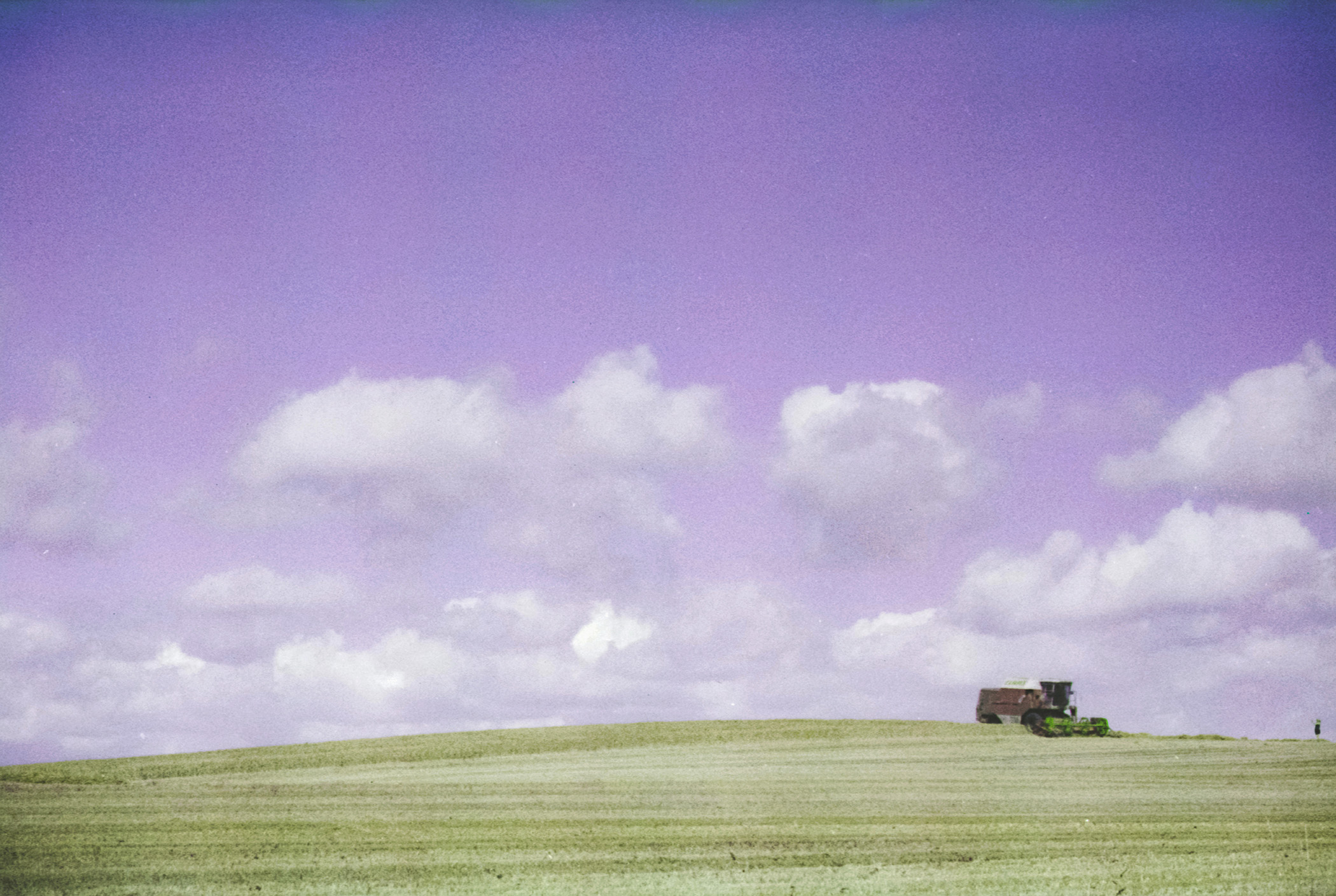Bucolicism — peak summer farmland in southern Sweden with a modern combine harvester atop a hill, shot on color-shift film.